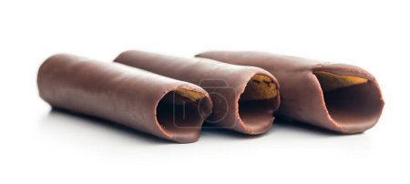 Rollos de oblea cubiertos de chocolate apilados uno encima del otro sobre un fondo blanco. Los rollos son de color marrón claro y están cubiertos con una fina capa de chocolate negro. Los rollos de oblea son ligeramente curvados y tienen una textura crujiente.