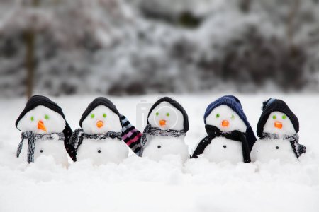 Foto de Lindos muñecos de nieve en una línea vestida con sombreros y bufandas en invierno con un fondo de nieve - Imagen libre de derechos