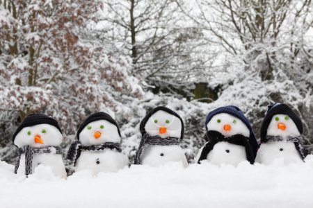 Téléchargez les photos : Petits bonhommes de neige avec des vêtements d'hiver dans la neige profonde à Noël. Nez de carotte et arbres couverts de neige regardent la caméra - en image libre de droit