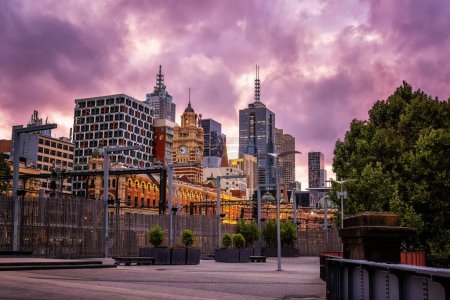 Paisaje urbano de Melbourne, con la estación de tren de Flinders Street en primer plano, al anochecer desde la pasarela a lo largo de las orillas del río Yarra. Luz rosada brillante del atardecer y cielo.