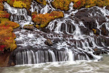 Hraunfossar or Lava Falls, Snaefellsnes peninsula, Iceland. This fairytale location sees multiple waterfalls cascading through volcanic rock. The autumn colours of yellow and red add to the magic.