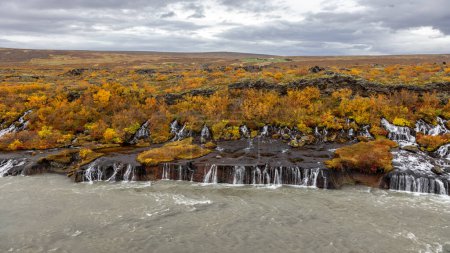 Hraunfossar or Lava Falls, Snaefellsnes peninsula, Iceland. This fairytale location sees multiple waterfalls cascading through volcanic rock. The autumn colours of yellow and red add to the magic.