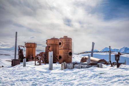 Maquinaria de minería de mármol abandonada en Camp Mansfield, New London, Svalbard. Fondo de montaña cubierto de nieve con cielo azul.