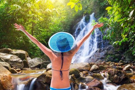 Foto de Mujer con sombrero disfrutando de las vacaciones de sol en la cascada en Tailandia - Imagen libre de derechos