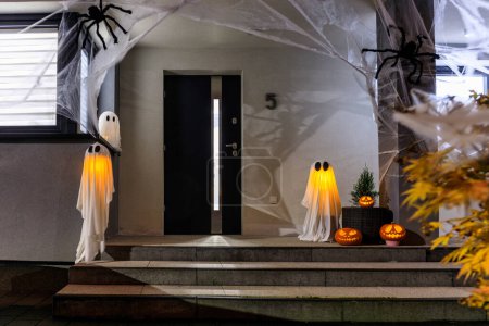 Téléchargez les photos : Effrayant Halloween citrouilles et fantômes luisant la nuit comme décoration sur les marches avant - en image libre de droit