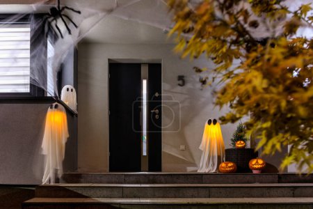 Foto de Espantosas calabazas de Halloween y fantasmas que brillan por la noche como decoración en los escalones delanteros - Imagen libre de derechos