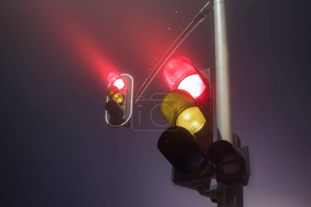 Traffic lights with red light during a foggy night.