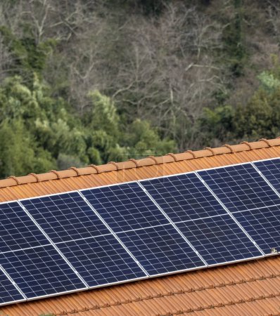 Instalación de mini paneles solares azules pequeños en un techo oscuro de una casa durante el día soleado en una ciudad de Polonia.