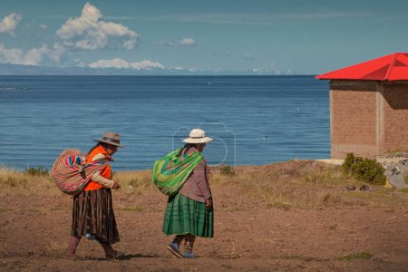Photo for AMANTANI ISLAND, PUNO, PERU, - 29 April 2022: Two Quechua indigenous women in traditional clothing and textile walking down the steps on Taquile island by the Titicaca Lake, Puno, Peru. - Royalty Free Image