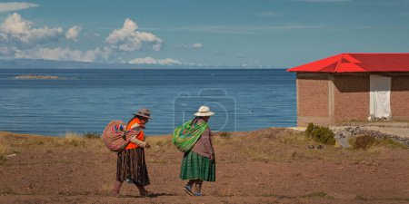 Photo for AMANTANI ISLAND, PUNO, PERU, - 29 April 2022: Two Quechua indigenous women in traditional clothing and textile walking down the steps on Taquile island by the Titicaca Lake, Puno, Peru. - Royalty Free Image