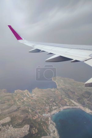 Wolken und ein Flügel des Wizzair-Airbusses aus dem Flugzeugfenster. über Maltas Inseln und dem Mittelmeer