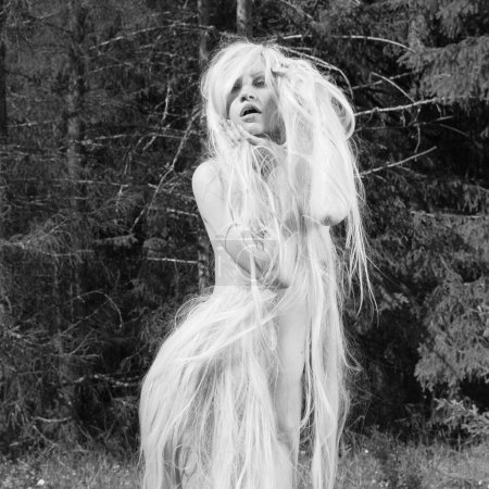 Foto de Beautiful naked girl with long hair. Model posing in the forest. Sexy blonde walks in nature. - Imagen libre de derechos