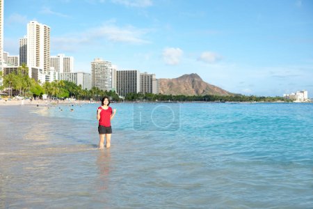 Foto de Mujer joven vadeando hasta las rodillas a lo largo de la playa de Waikiki y Kuhio, Oahu, Hawai con el cráter Diamond Head en el fondo - Imagen libre de derechos