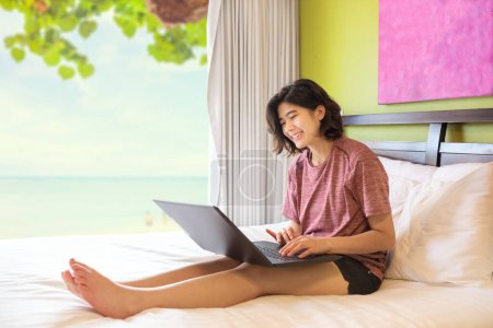 Photo for Young woman or teen sitting up on bed using laptop computer - Royalty Free Image