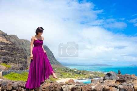 Photo for Young woman in formal purple dress standing at Makapu'u Viewpoint overlooking Makapu'u beach and Hawaiian ocean on Oahu, Hawaii - Royalty Free Image