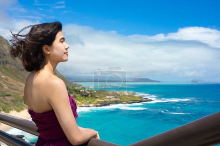 Junge Frau in formalem lila Kleid am Makapu 'u Aussichtspunkt mit Blick auf den Makapu' u Strand und den hawaiianischen Ozean auf Oahu, Hawaii