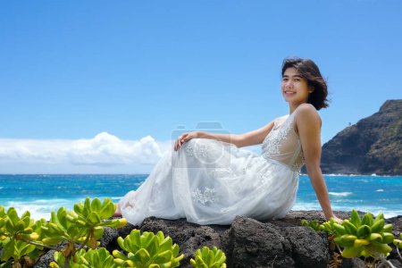 Foto de Chica adolescente en vestido blanco sentado en rocas de lava a lo largo de la costa hawaiana en la playa de Makapu 'u - Imagen libre de derechos