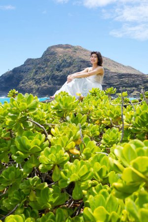 Foto de Chica adolescente en vestido blanco sentado en rocas de lava a lo largo de la costa hawaiana en la playa de Makapu 'u - Imagen libre de derechos