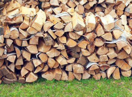 Photo for Stacked firewood for bbc on green grass of yard, background woodpiles of firewood.  Stocks of firewood for the winter, for barbeque, fuel, energy - Royalty Free Image