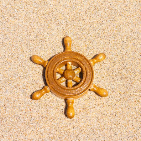 Foto de Rueda del barco de recuerdo descansando en la playa de arena, una pieza de decoración de temática náutica sobre el telón de fondo de la orilla del mar - Imagen libre de derechos