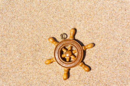 Photo for Souvenir ship's wheel resting on the sandy beach, a nautical-themed decor piece against the backdrop of the seashore - Royalty Free Image