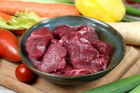 Photo for Raw deer meat for venison ragout or goulash.  Bowl with pieces of deer meat on cutting board, fresh vegetable for cooking around. - Royalty Free Image