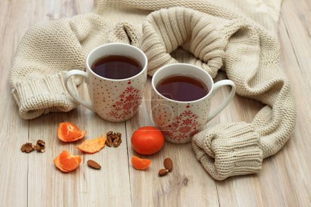 Photo for Winter concept with tea for two, sweater and tangarines. Two big mugs with tea surrounded by warm knitten sweater on wooden table. - Royalty Free Image