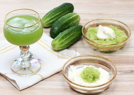 Photo for Several ways to prepare a facial mask and a delicious juice from cucumbers at home. Cucumbers and yogurt for smoothing, softening and hydrating skin and cucumber  drink in glass decorated with gold. - Royalty Free Image