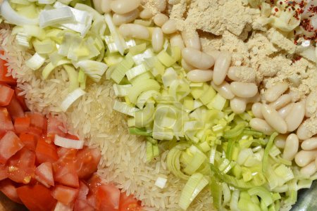 Vorbereitung einer veganen Mahlzeit aus Tomaten, Reis, Lauch, weißen Bohnen, Zwiebeln, Knoblauch, Nährhefe und Gewürzen