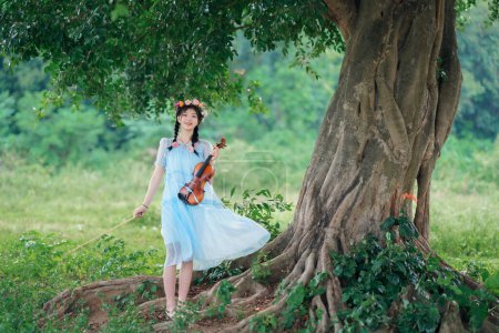 The girl is playing the violin under the big tree