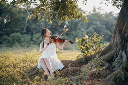 Photo for The girl is playing the violin under the big tree - Royalty Free Image