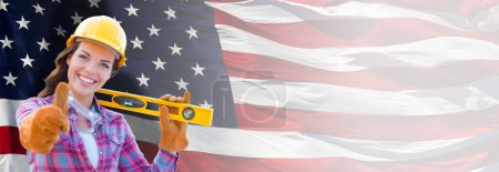 Photo for Female Contractor Wearing Blank Yellow Hardhat and Gloves Over Waving American Flag Background Banner. - Royalty Free Image