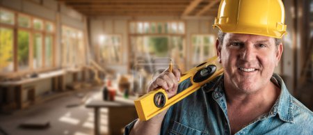 Téléchargez les photos : Heureux entrepreneur masculin sur un chantier de construction portant un chapeau dur et des gants de travail tenant son niveau. - en image libre de droit