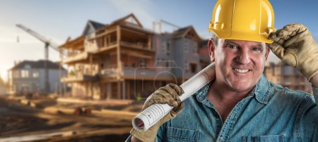 Téléchargez les photos : Entrepreneur masculin amical sur un chantier de construction portant un casque protecteur et des gants de travail tenant son plan directeur - en image libre de droit