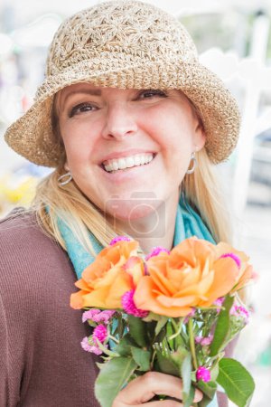 Foto de Mujer rubia pequeña con sombrero sosteniendo un ramo floral recién cortado en el mercado de agricultores. - Imagen libre de derechos