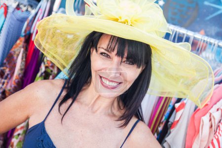 Foto de Sonriente morena mujer modelando un gran sombrero de sol en el mercado. - Imagen libre de derechos