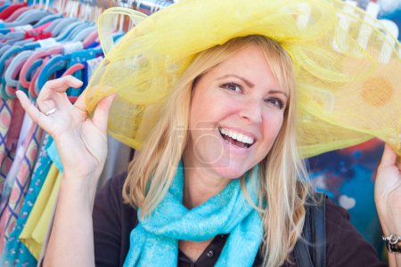 Foto de Mujer rubia feliz modelando juguetonamente un sombrero grande del sol en el mercado. - Imagen libre de derechos