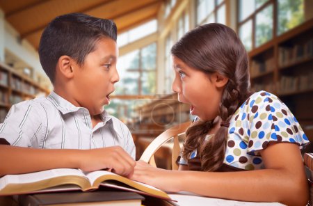 Foto de Dos niños de escuelas hispanas en una biblioteca con una expresión impactada en la cara - Imagen libre de derechos