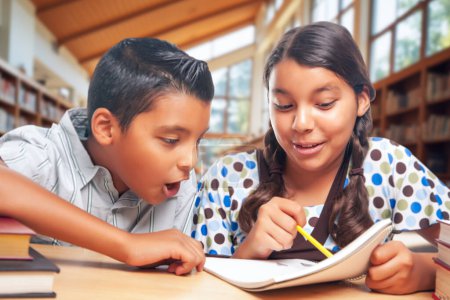 Téléchargez les photos : Les écoliers hispaniques font leurs devoirs ensemble à la bibliothèque. - en image libre de droit