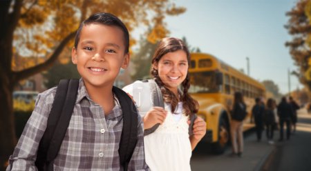 Foto de Feliz joven hispano y niña usando mochilas cerca de un autobús escolar en el campus - Imagen libre de derechos