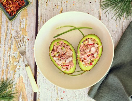 Diet conscious avocado tuna boats with chopped green onion, radish and red pepper flakes for a healthy protein packed meal.  Flat lay composition in horizpntal format.
