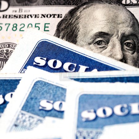Several Social Security Cards on a US United States one hundred dollar bill $100 system of benefits for retired elderly people