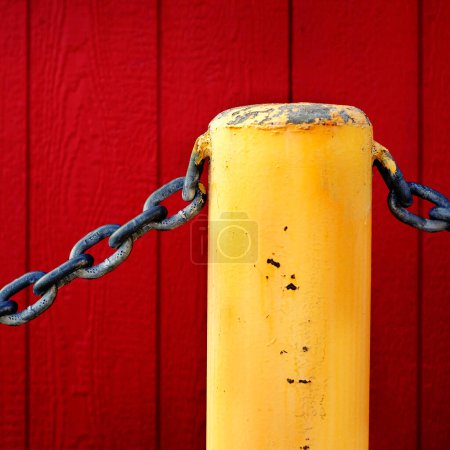 Heavy chain and yellow pole for safety and security with red wall in the background