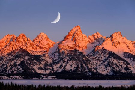 Morgendliches Sonnenaufgangslicht auf dem Teton Mountain Massiv in Wyoming Alpen leuchtet orange und rosa auf schroffen Bergen mit Halbmond