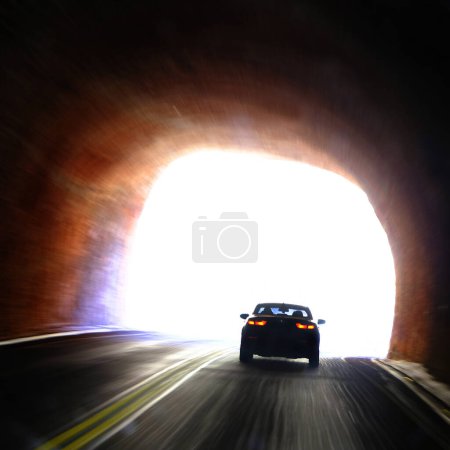 Car driving through dark tunnel and entering light of freedom