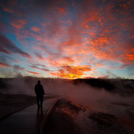 Téléchargez les photos : Lever de soleil près de Yellowstone geysers avec vapeur et silhouette de personne sur la promenade - en image libre de droit