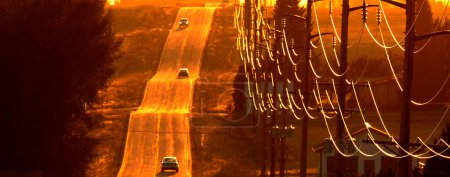 Téléchargez les photos : Voitures conduisant sur la vieille route de campagne au coucher du soleil des lignes électriques de lever du soleil - en image libre de droit