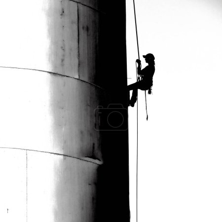 Silhouette of professional person on ropes dangling in air painting sign on side of building silo