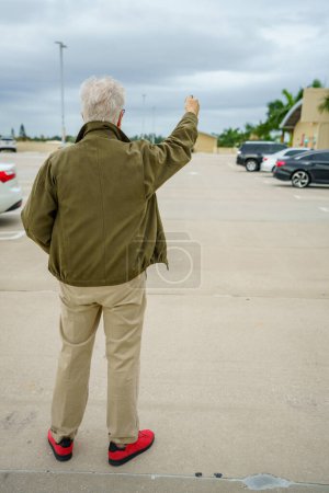 Téléchargez les photos : Old man looking for his car in a parking lot by pushing the unlock button on his fob - en image libre de droit
