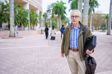 Foto de PHoto of a college professor walking on campus with blurry people in background - Imagen libre de derechos